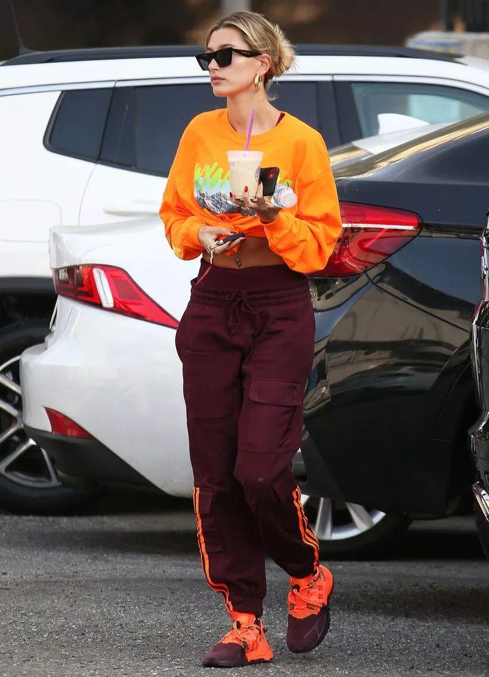 Bà xã Justin Bieber ăn diện cực thời thượng với những item gam màu nổi như sweater cam thắt eo và jogger viền đỏ đô. (nguồn ảnh: Internet)
