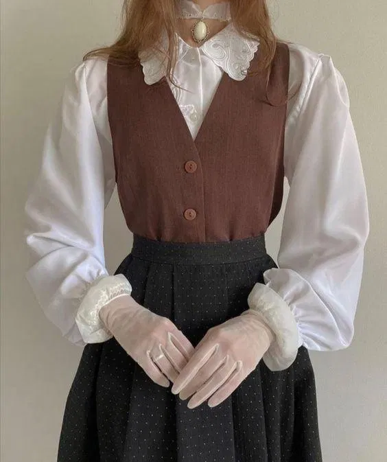 Sơ mi trắng kết hợp với gile vest nâu, phối thêm chân váy đen chấm bi là lựa chọn đem tới nét cổ điển đầy dịu dàng. (Nguồn: Internet).