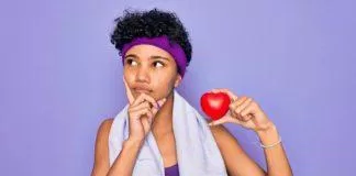 Beautiful african american afro sporty woman doing exercise wearing towel holding heart serious face thinking about question, very confused idea