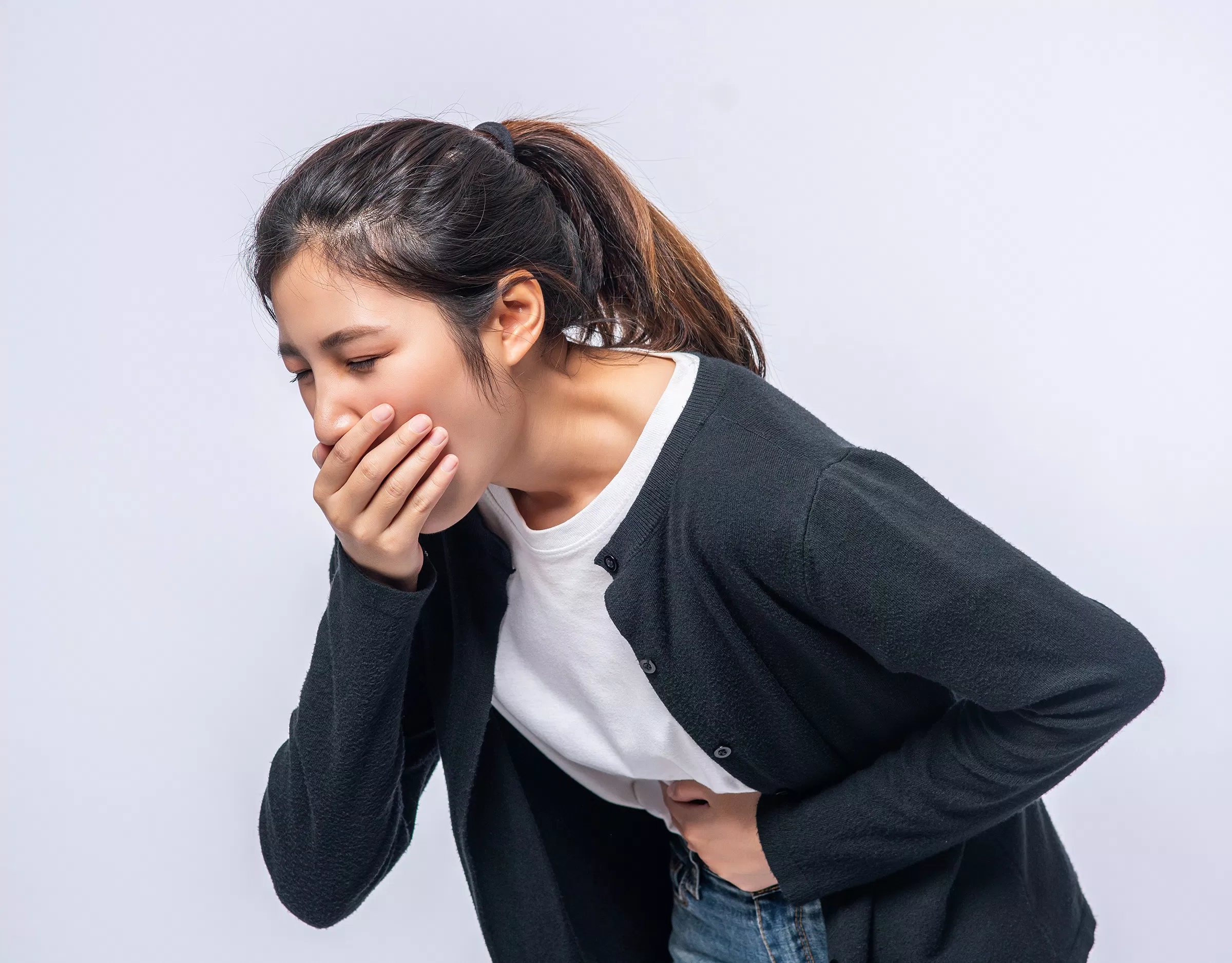 A woman with a stomachache puts her hands on her stomach and covers her mouth.