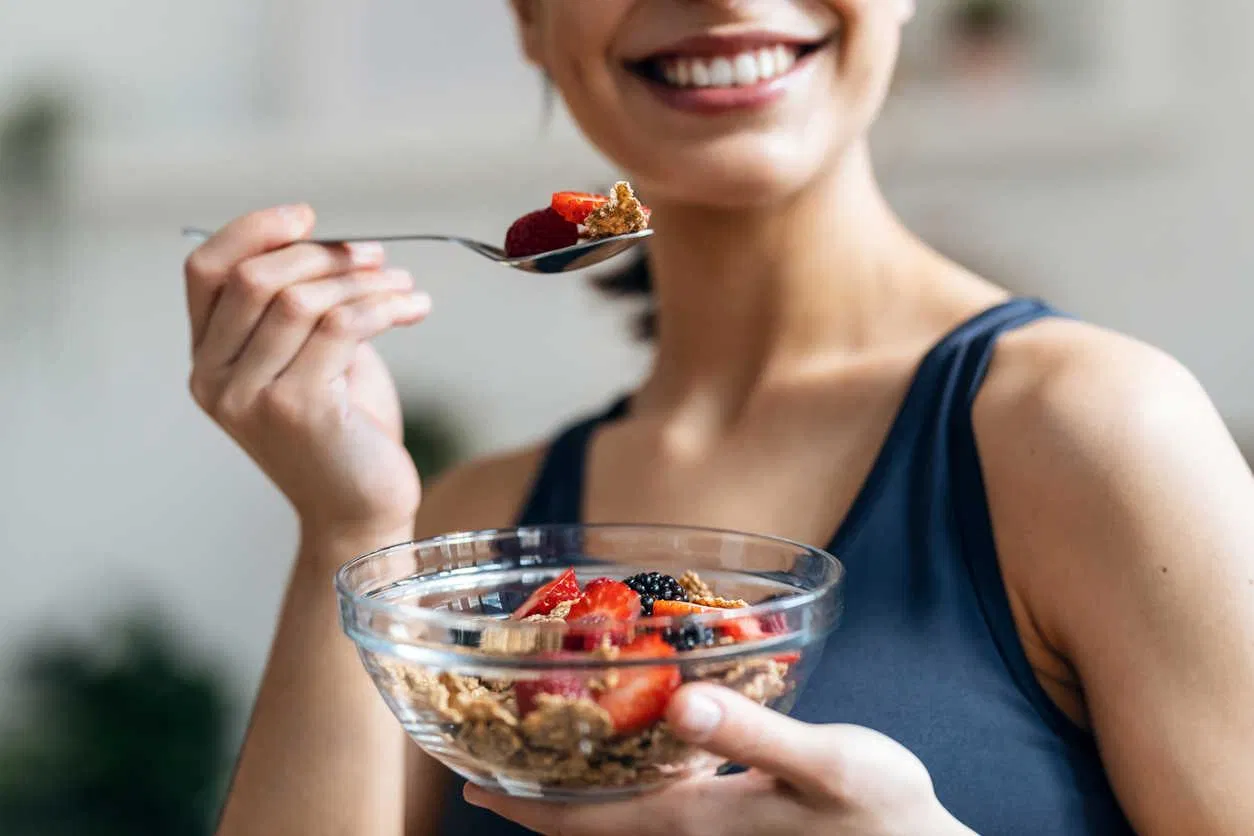 Shot of athletic woman eating a healthy bowl of muesli with fruit in the kitchen at home